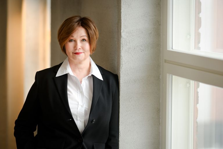 Milla Bruneau nojaa seinään päällään tumma jakku ja valkoinen paita.