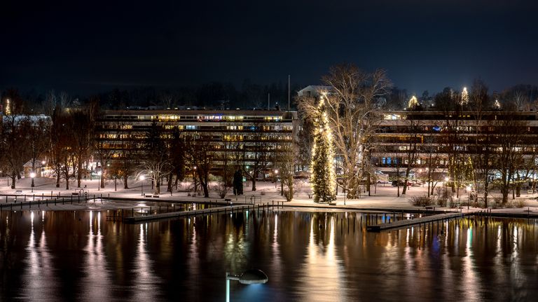 The city of Heinola in evening light. In the foreground, water reflecting the lights of the apartment buildings in the background.