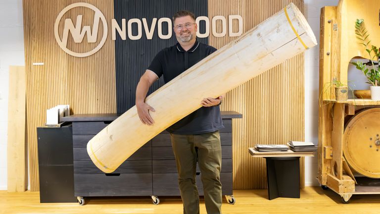 Novo Woodin toimitusjohtaja Jarkko Puska pitää sylissää jättimäisen isoa kuorittua tukkia / puunrunkoa.